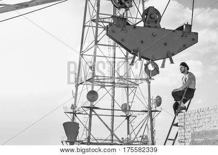 Old fashioned builder. Thoughtful retro styled handy man resting on top of the ladder at the building under construction industry crane worker profession job monochrome fearless high concept copyspace