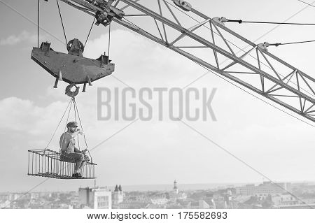 Having a break. Retro styled shirtless handyman drinking milk relaxing sitting on a crossbar hanging from a crane at construction site. copy space. monochrome