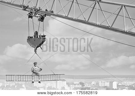 Black and white shot of a fearless retro builder reading a newspaper sitting high above the city on the crossbar at construction site. copy space.