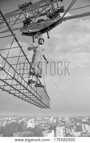 Fearless worker. Vertical low angle monochrome shot of a professional handyman working at construction site standing on a crossbar hanging from a construction crane. development builder industry.