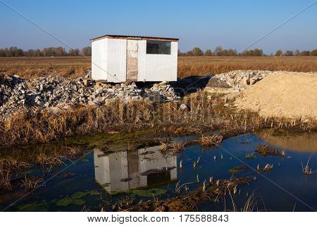 Old abandoned white plastic shed near the mud.