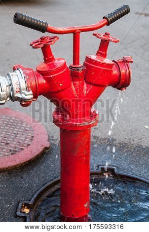 Red fire hydrant in the open manhole with connected hose. Close-up.