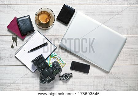 View of a wooden table with a laptop, external hdd, mobile, notebook, camera, pen, watch, wallet, passport, map, keys and a cup of coffee on it