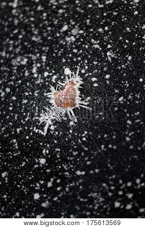 Heart shaped leaf covered with frost over frozen black ice background with snowy stars. Broken heart. Frosty scene.