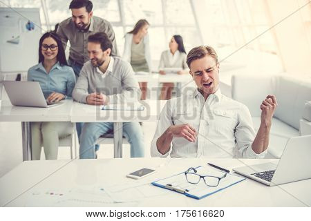 Business people are using gadgets talking and smiling while working in office. Guy in the foreground is listening to the music and imitating guitar