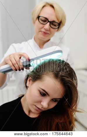 Doctor examines scalp a pretty young girl with special instrument UV lamp. Skin problems, dermatology, shingles, psoriasis, redness, prevention