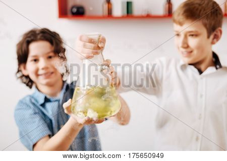 New chemical discovery. Selective focus of a chemical flask being filled with liquid while being in hands of nice intelligent happy boys