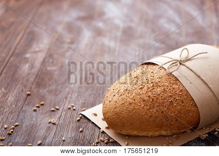 White bread in the baking paper and decorative rope on the wooden table, selective focus. Brown background. Table with flour and whole. Natural products and materials. Baker and tasty.
