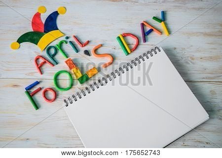 April Fools' Day text made with plasticine and free sapce on note on white wooden background