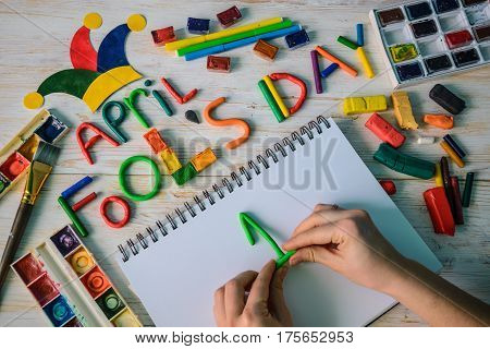 hands make April Fools' Day text made with plasticine on white wooden background