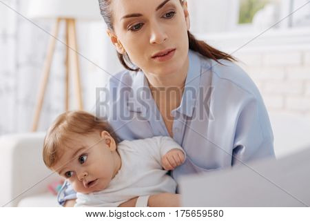 What is it out there. Adorable restless little child wanting doing something with her mom while she reading a report for her work
