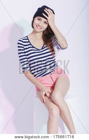 Youth fashion Concepts and Ideas. Happy Stylish Smiling Caucasian Slim Brunette in Hat Posing On White Box in Studion Against White. Vertical Composition
