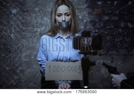 Say cheese. Weak powerless rich girl holding a sign with a sum which one paying for her staying alive