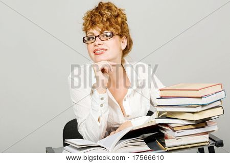 Attraktiva rödhårig dam sitter vid skrivbord med böcker stack