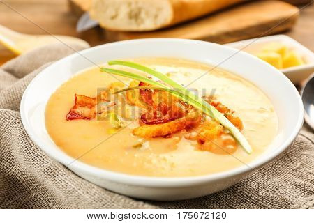 Delicious beer cheese soup with onion and fried bacon on table