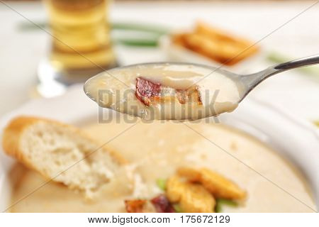 Spoon with delicious beer cheese soup and fried bacon, close up