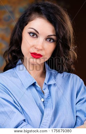 Closeup portrait of young brunette woman in blue shirt, dark studio wall background