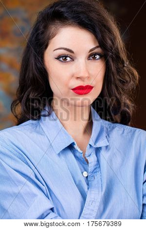Closeup portrait of young brunette woman in blue shirt, dark studio wall background