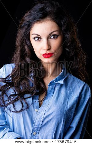 Closeup portrait of young brunette woman in blue shirt, dark studio wall background