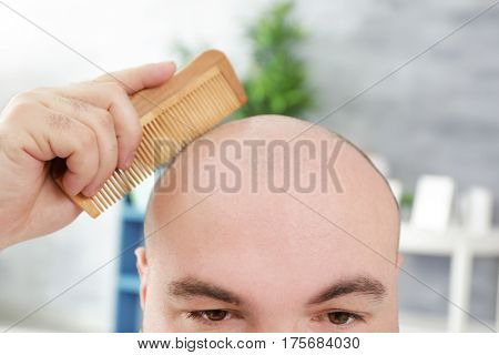 Bald adult man with comb on blurred background, closeup