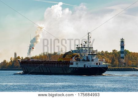Black cargo ship with long reach excavator moving by Baltic sea