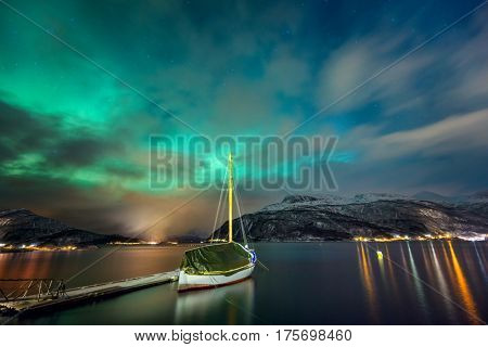 Northern lights in the Norwegian fjord and the yacht. The landscape of the Northern nature. Winter. Mountains covered with snow