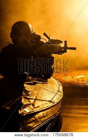 Backlit silhouette of special forces marine operators in military kayak on fire explosion background. Battle operation