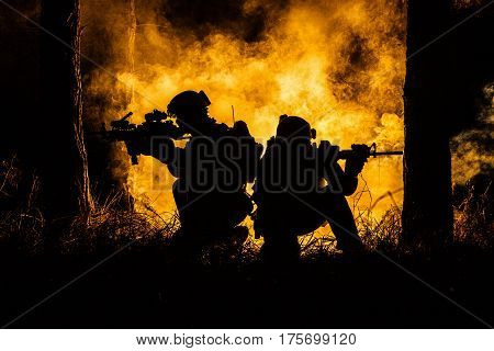 Backlit silhouette of special forces marine operators in forest on fire explosion background. Battle, bombs exploding, they fighting no matter what