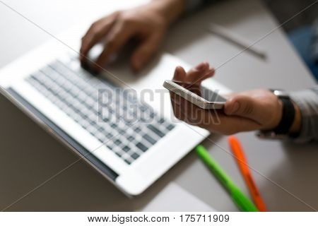 Man holding Telephone in front of Laptop in dark warm tones with focus on edge of phone