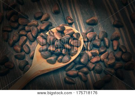 Cedar seed nuts and spoon on wooden background. Vintage toned