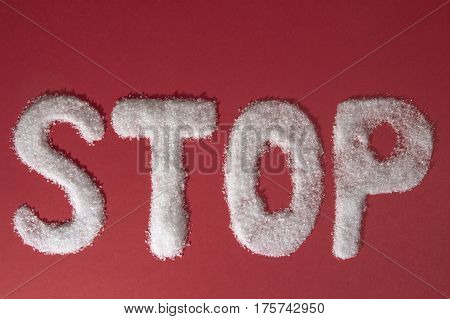 The word STOP written by sugar grains on red background. Top view