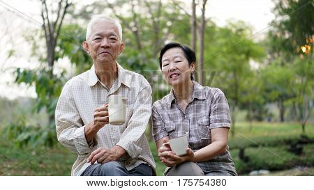 Old Asian Senior Couple Morning Date With Cup Of Coffee In Green Background Park