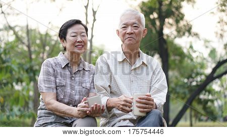 Old Asian Senior Couple Morning Date With Cup Of Coffee In Green Background Park