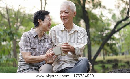 Old Asian Senior Couple Morning Date With Cup Of Coffee In Green Background Park