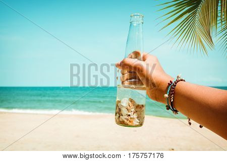Relaxation and Leisure in summer - Young tanned women hand holding bottle with seashell at tropical beach in summer. vintage color tone effect
