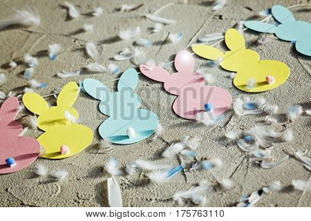 Garland with colorful paper rabbits and fethers on concrete background. Concept Easter Bunny Banner. Top view.