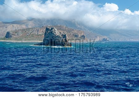 The rocky coast of the Mediterranean sea against the blue sky and clouds.