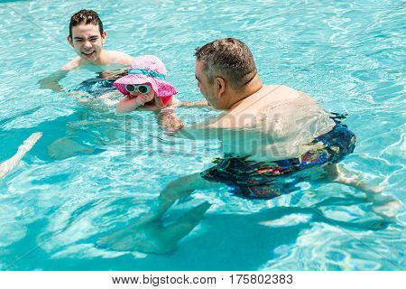 Family with cute baby girl faving fun in outdoor swimming pool on hot summer day.