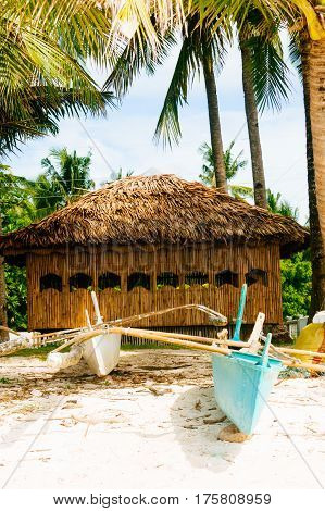 Native nipa hut with small fishing boats in front on beautiful white sand beach