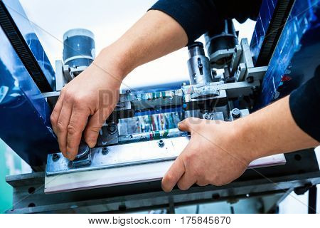 Worker preparing print screening metal machine. Industrial printer. Manufacture work.
