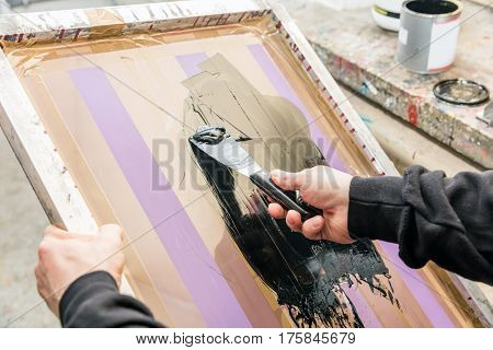 Man squeegeeing silkscreen in a workshop. Serigraphy industry. Manufacture work.