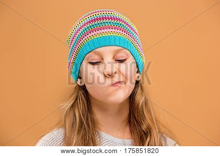 The face of unhappy sad teen girl in hat on brown studio background