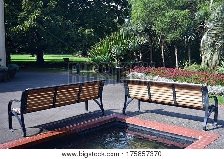 two park benches on sunny day at right angles in front of pond