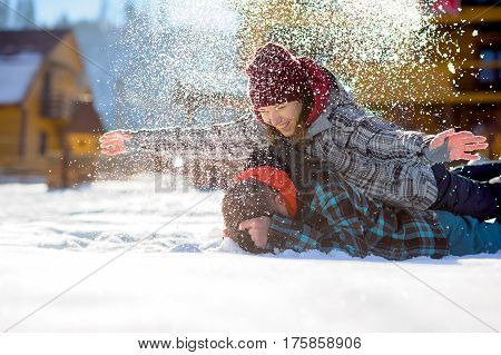 Young couple lies on the snow. The girl climbed onto the back of her boyfriend and sprinkled it with snow. Between them comic fight. Sunny winter day. Good mood. Young people smile