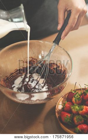 Woman chief filling milk into glass bowl. Preparing for bakery with strawberries.