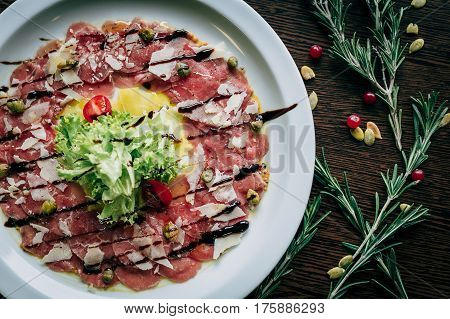 Salad of veal carpaccio in a white plate close-up on a wooden table