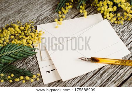 Vintage post cards mock up with yellow flowers mimosas and vintage pen ink on grey wooden background. Overhead view. Flat lay, top view, moke up