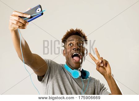 young afro american black man smiling happy taking selfie self portrait picture with mobile phone looking excited having fun posing cool isolated in grey background in communication technology