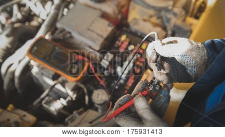 Mechanic works with car electrics - electrical wiring, voltmeter, close up