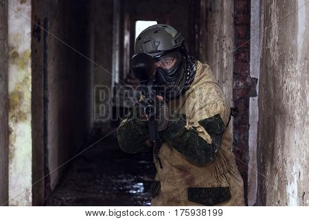 Shot of militaty man takes aim in lense with paintball weapon